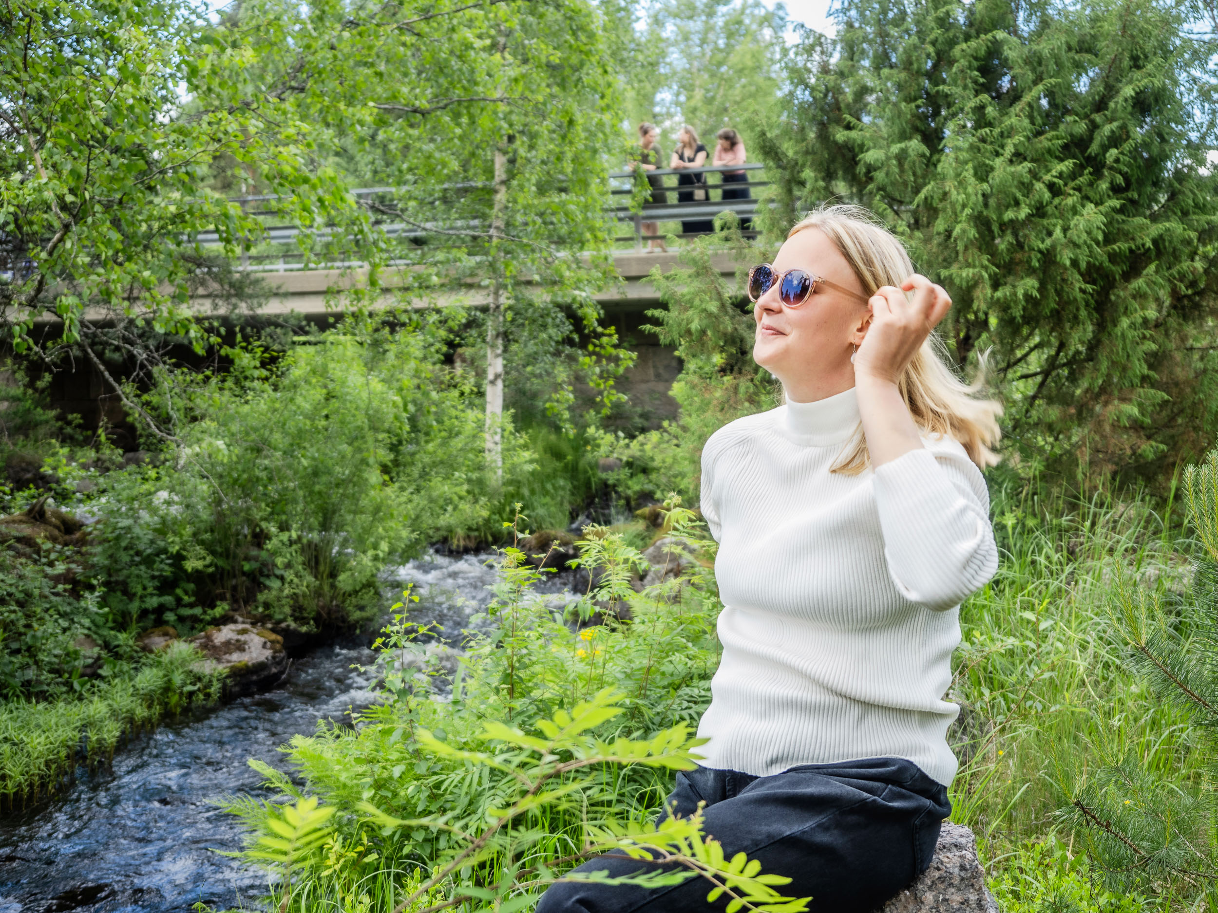 Nainen nauttimassa kesästä kosken vieressä kivellä